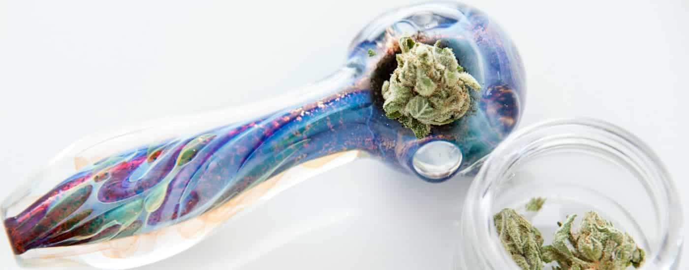 A colorful glass bowl is shown packed with marijuana, which is a popular method on how to consume cannabis.