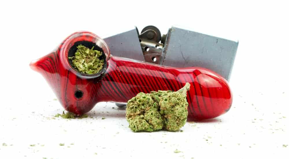 A red pipe is shown with cannabis and a lighter.