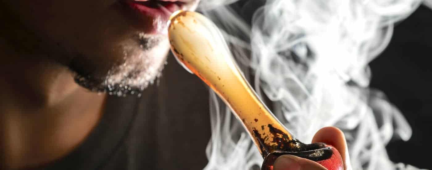 A closeup of a mans smoking from a glass pipe is shown.