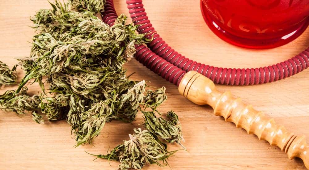 Cannabis is shown next to a red and wooden mouth piece from a red hookah.