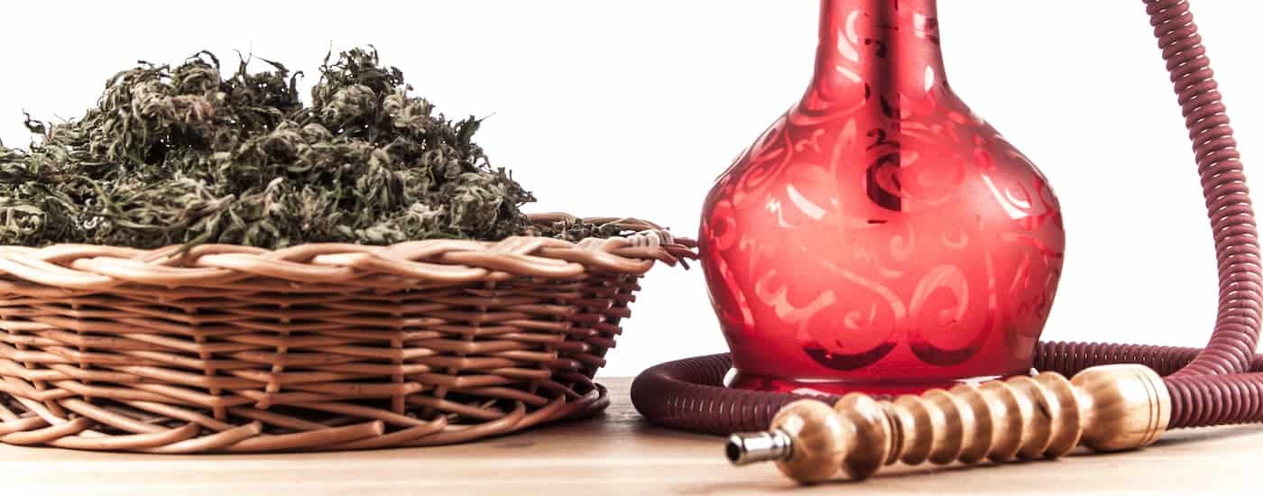 Cannabis in a basket is shown next to a red and wooden mouth piece and a red hookah.