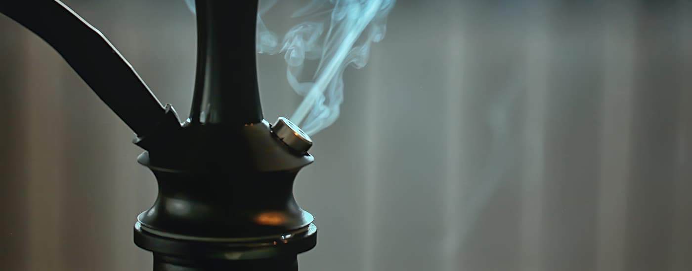 A closeup of smoke leaving a dark hookah is shown.