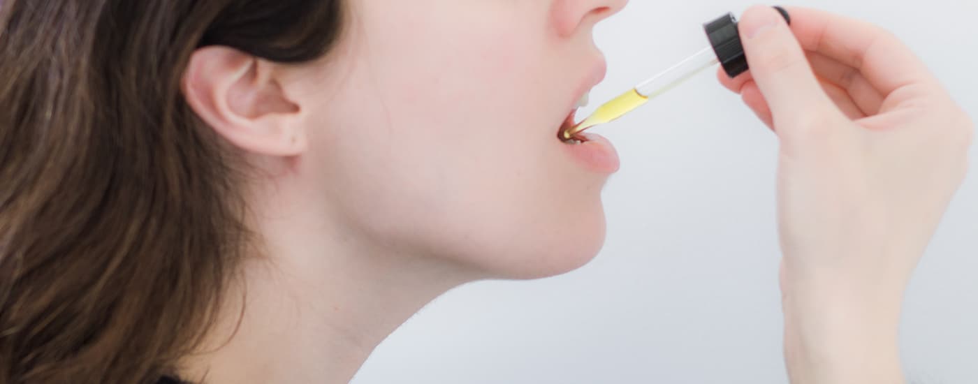 A woman is using a dropper to ingest CBD oil sublingually.