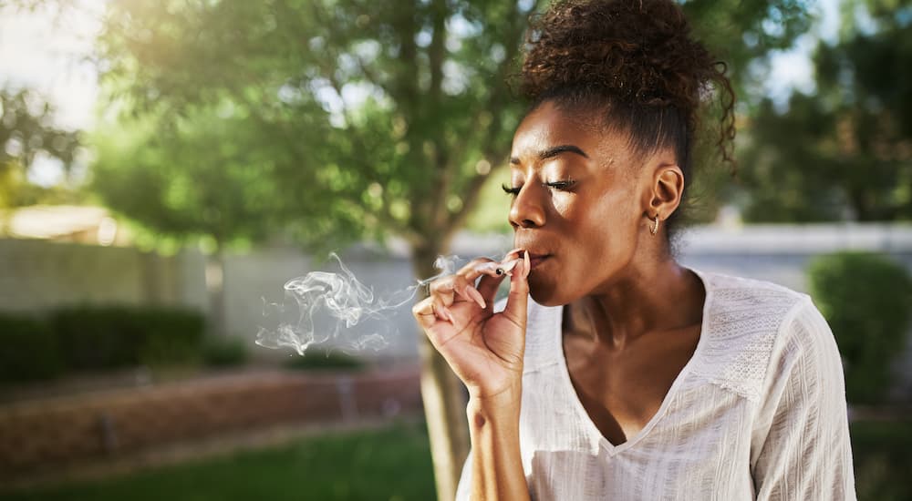 A woman is happily smoking cannabis in the sunshine in her yard.