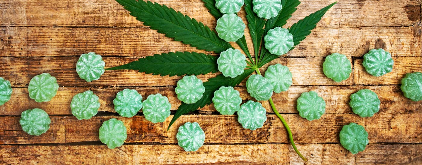 Green edible candies are shown over a cannabis leaf.