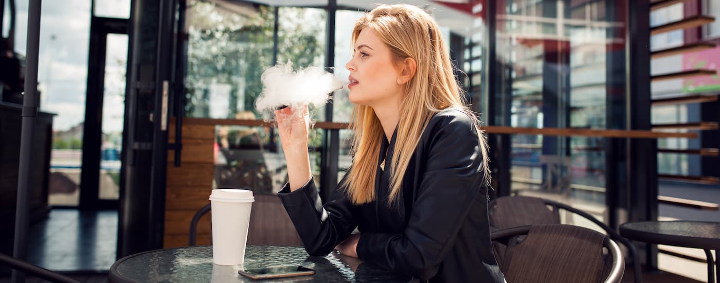 A woman is vaping outside a cafe.