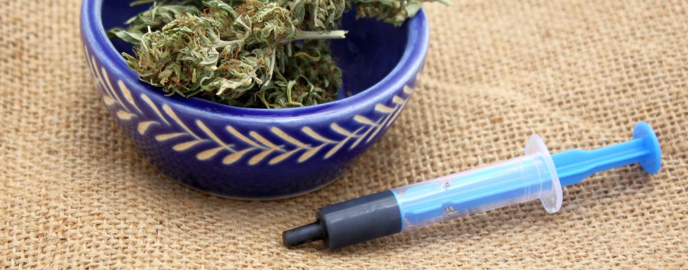 A blue syringe with Rick Simpson Oil is next to a bowl with cannabis.