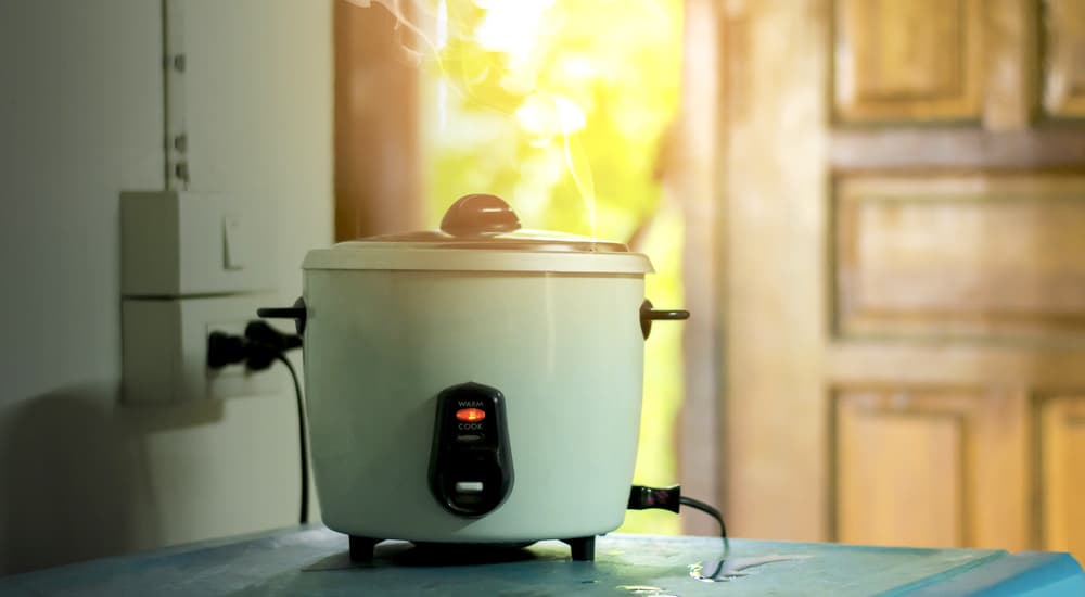 A rice cooker is steaming next to an open door.