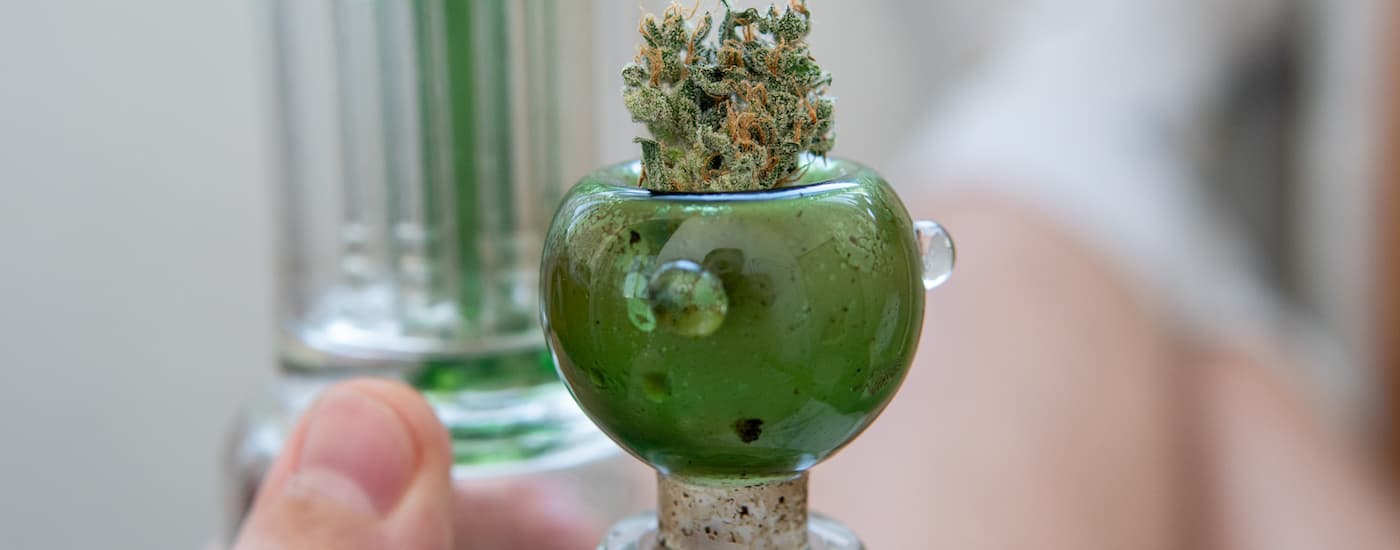 Cannabis is shown in the bowl portion of a green glass water pipe.